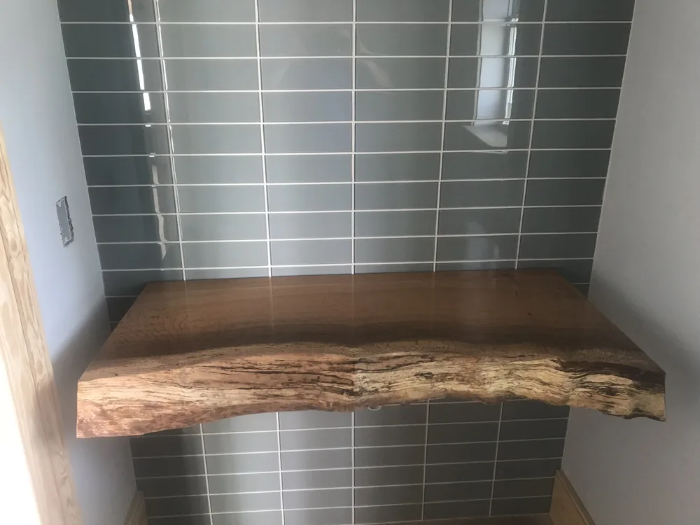 Glass tile accent wall with a live-edge wood shelf by Creative Construction Concepts